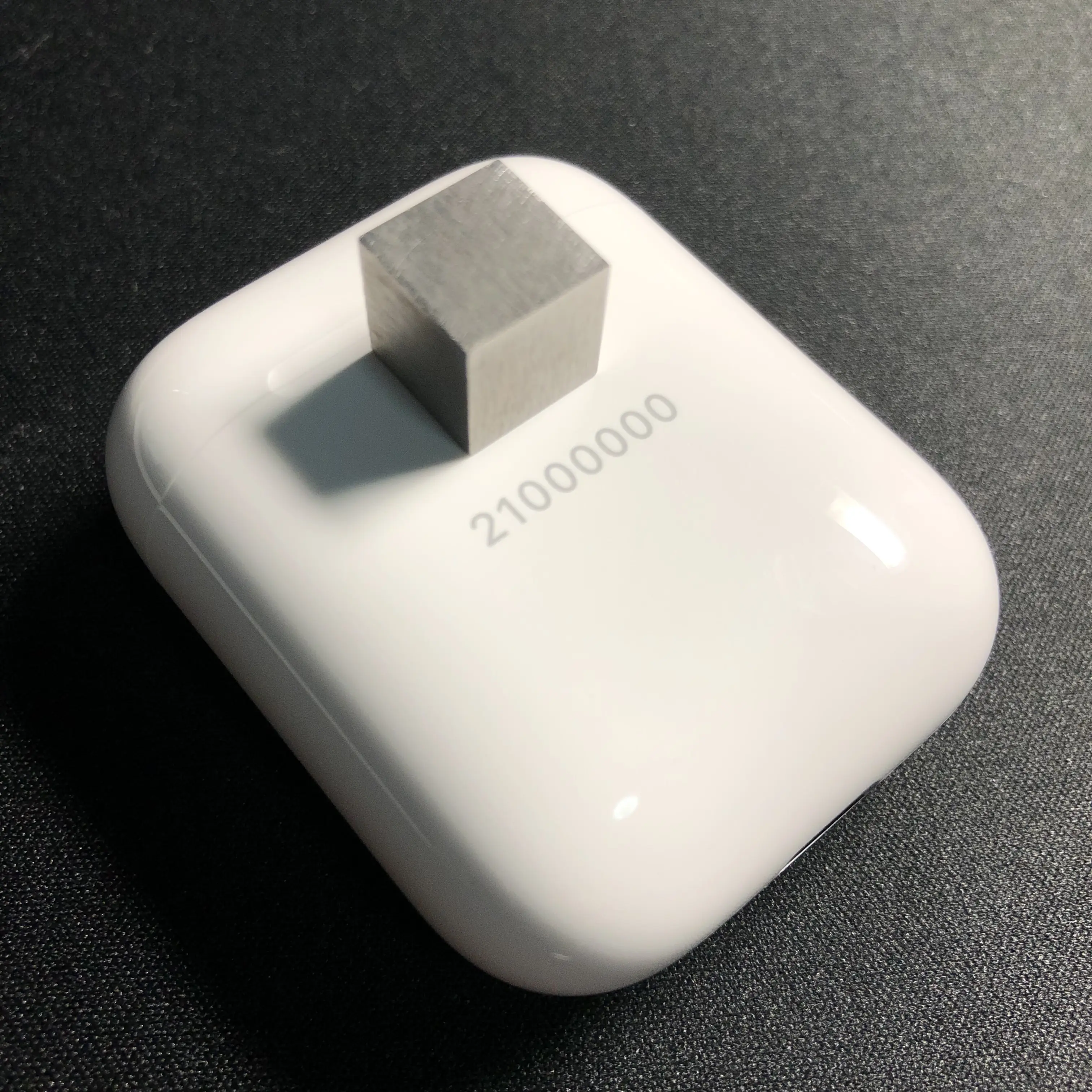 放置于AirPods充电盒上方的1cm*1cm*1cm钨块；AirPods的激光镌刻信息为“21000000”